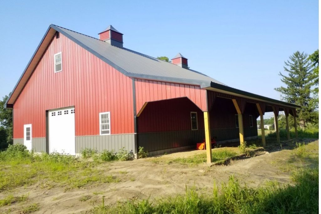 New garage with high pitched roof, red siding, and cupolas Spacious two-tone garage with overhang and metal roof